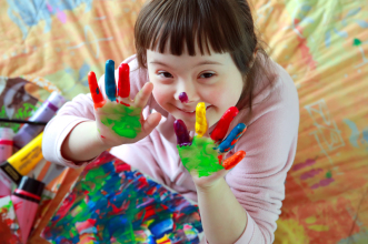 Kind mit Trisomie 21 zeigt ihre farbverschmierten Hände